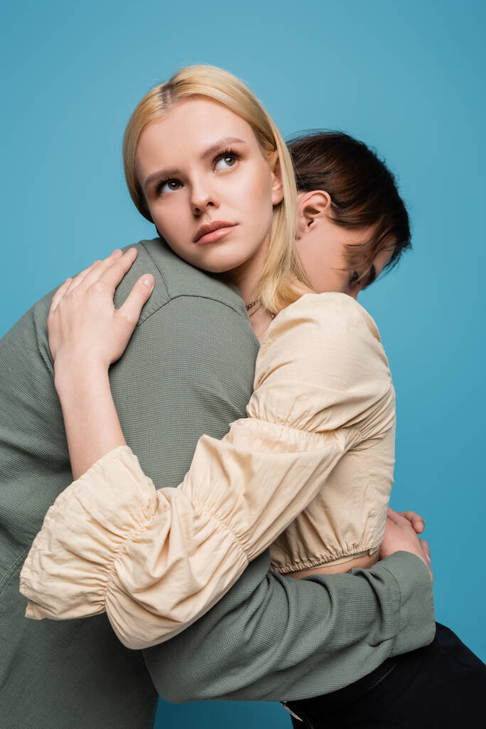 Mujer rubia bonita abrazando novio aislado en azul  - Foto, imagen