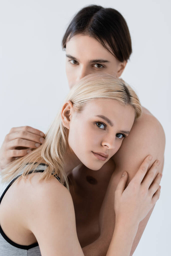 Mujer joven abrazando novio sin camisa y mirando a la cámara aislada en gris  - Foto, Imagen