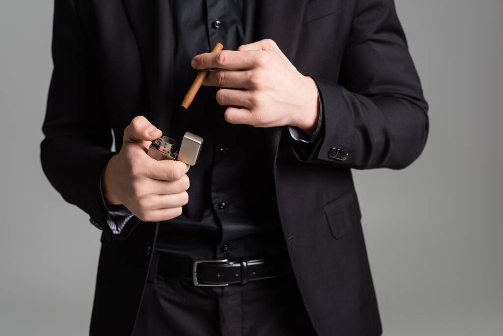 przycięty widok człowieka w czarnym formalnym ubraniu z zapalniczką i cygarem odizolowanym na szaro - Zdjęcie, obraz