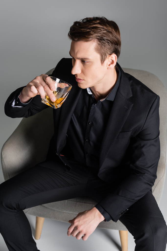 vysoký úhel pohledu na zamyšlený muž pití whisky a odvrací pohled na šedé pozadí - Fotografie, Obrázek