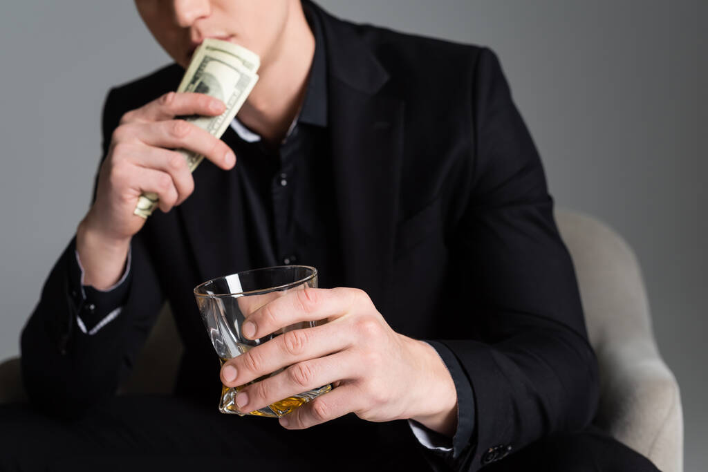 cropped view of blurred man with dollars and glass of whiskey isolated on grey - Fotografie, Obrázek