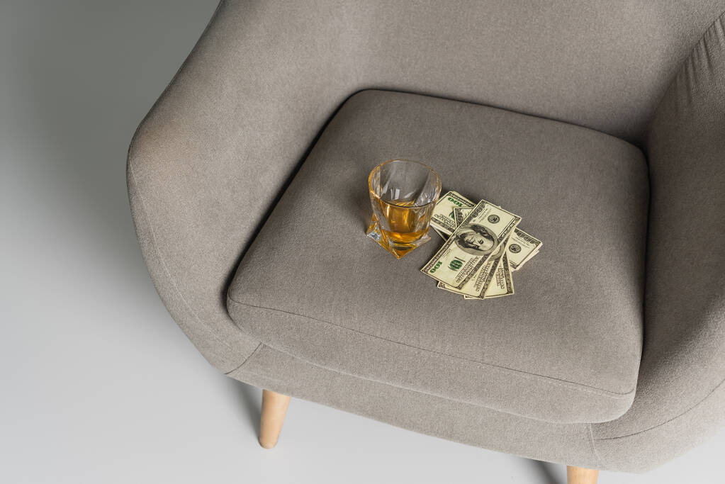 top view of dollar banknotes and glass of whiskey on grey armchair - 写真・画像
