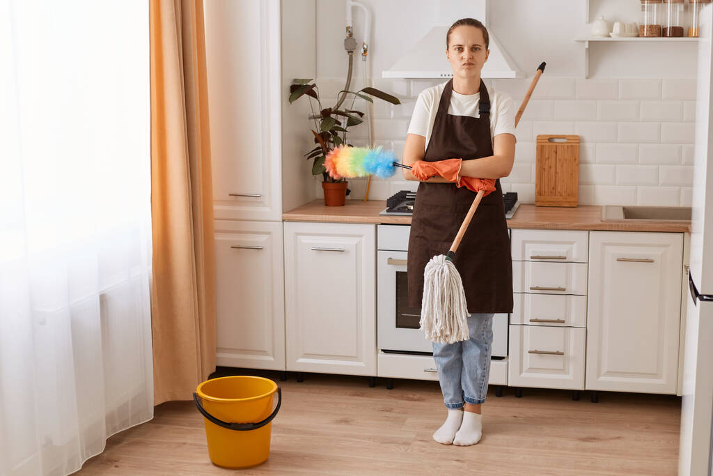 Retrato de larga duración de ama de casa cansada lavando el piso en la cocina, bonita mujer joven haciendo limpieza en casa, manteniendo su apartamento ordenado, sintiéndose sobrecargado de trabajo, mirando a la cámara. - Foto, Imagen