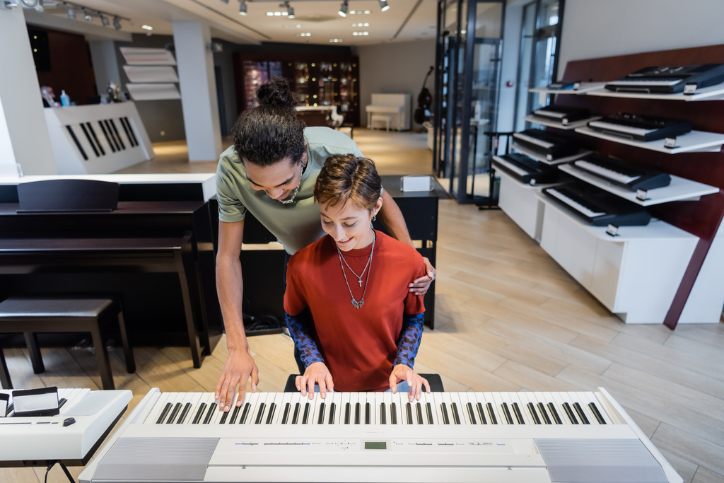 Smiling multiethnic couple playing synthesizer together in music store  - Photo, Image