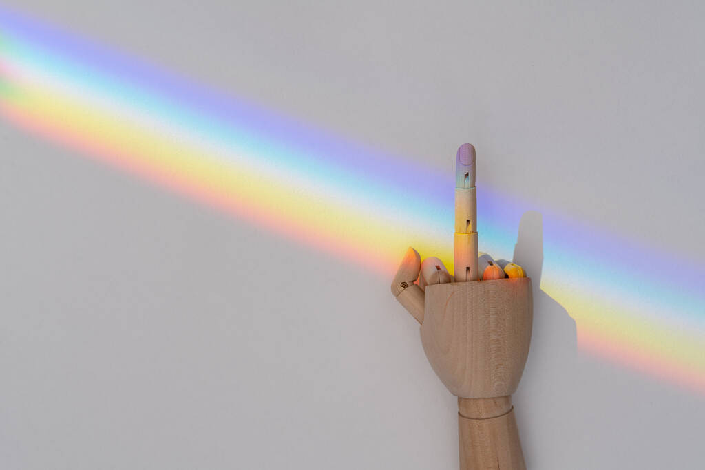 Wooden hand showing fuck you gesture on LGBT community rainbow flag background on a white background. LGBT community support and tolerance concept - Foto, Bild