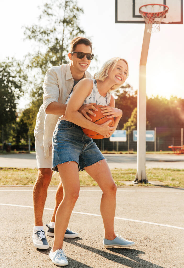 letní prázdniny, sport a lidé koncept - šťastný mladý pár s míčem hraje na basketbalovém hřišti - Fotografie, Obrázek