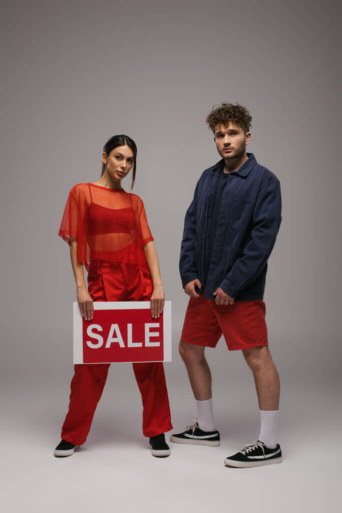 full length of young woman holding paper with sale lettering near man on grey - Foto, imagen