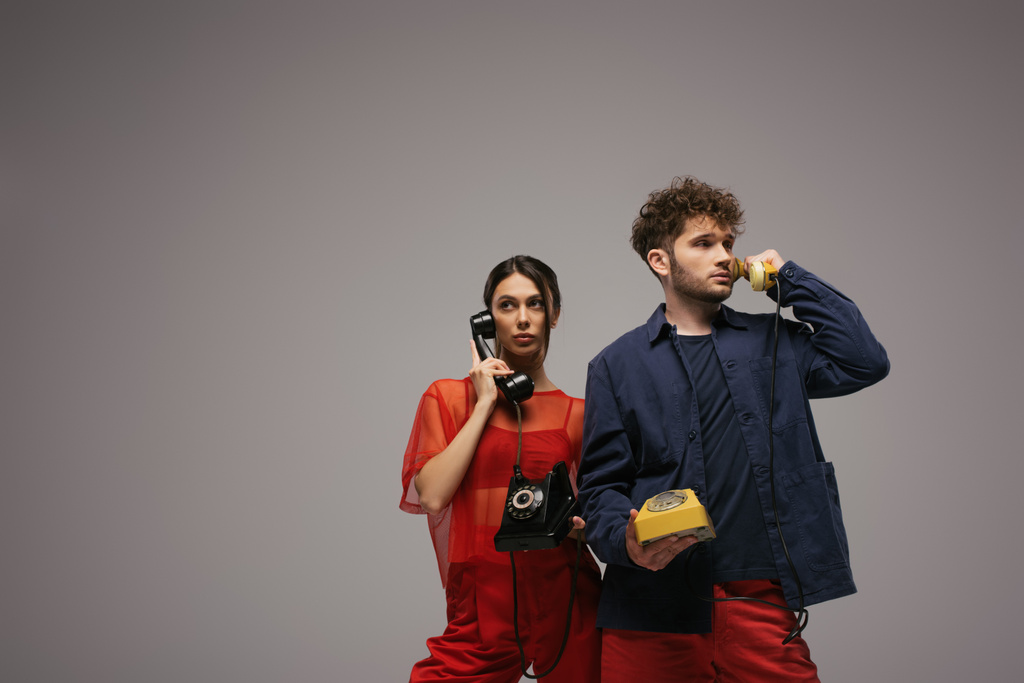 stylish young couple holding handsets and telephones isolated on grey - Zdjęcie, obraz