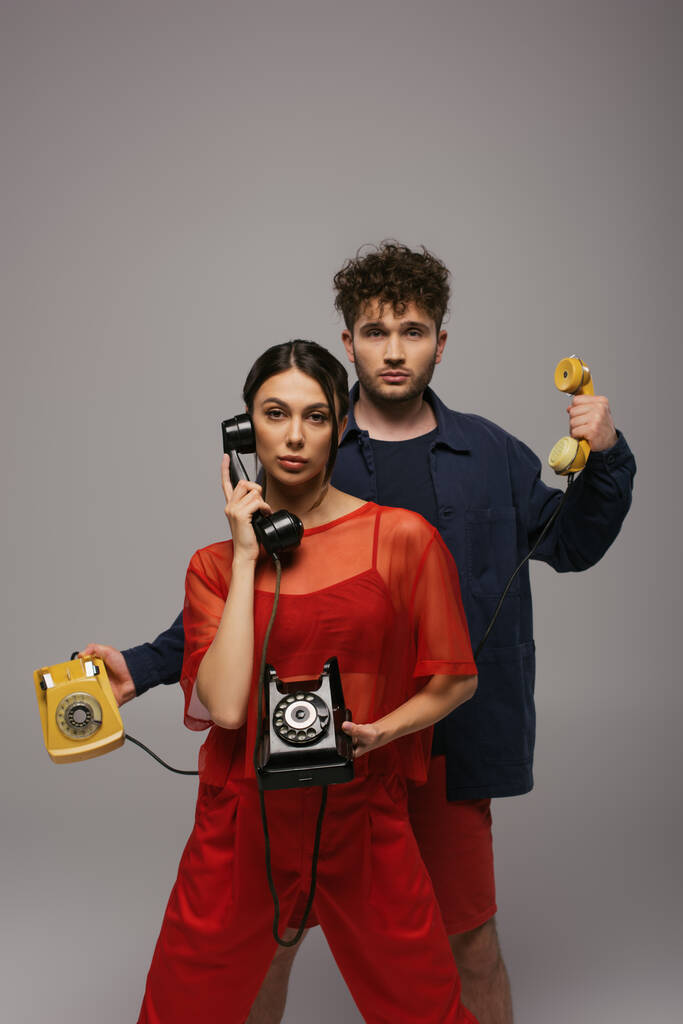 молода жінка і кучерявий чоловік тримає ретро телефони і ізольовані на сірому
 - Фото, зображення