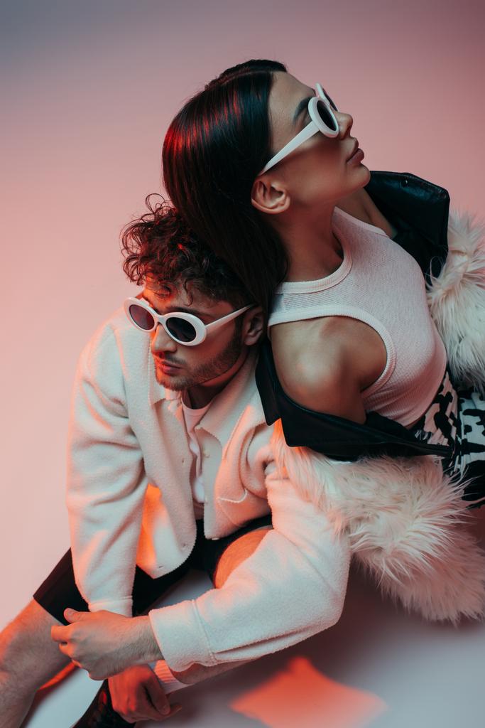 high angle view of stylish man in sunglasses and woman in faux fur jacket sitting on pink and grey - Φωτογραφία, εικόνα