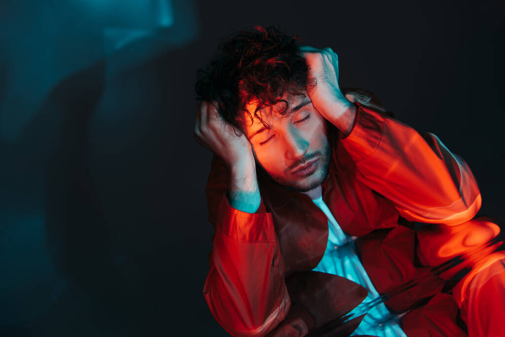 curly and stylish man with closed eyes posing in orange shirt on blue - 写真・画像