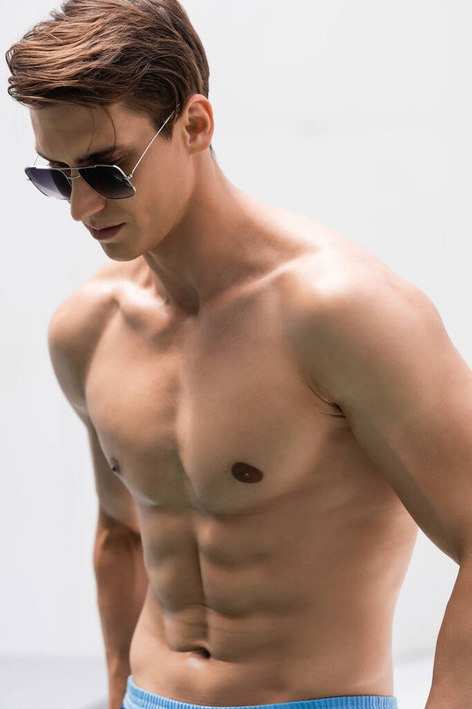Мужчина без рубашки с мускулистым туловищем в солнечных очках на белом фоне - Фото, изображение