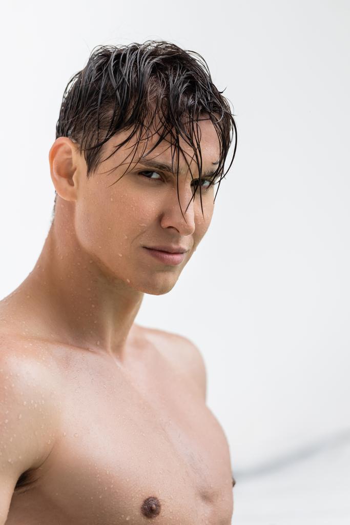 мокрый спортивный мужчина с идеальной кожей смотрит на камеру на белом фоне - Фото, изображение