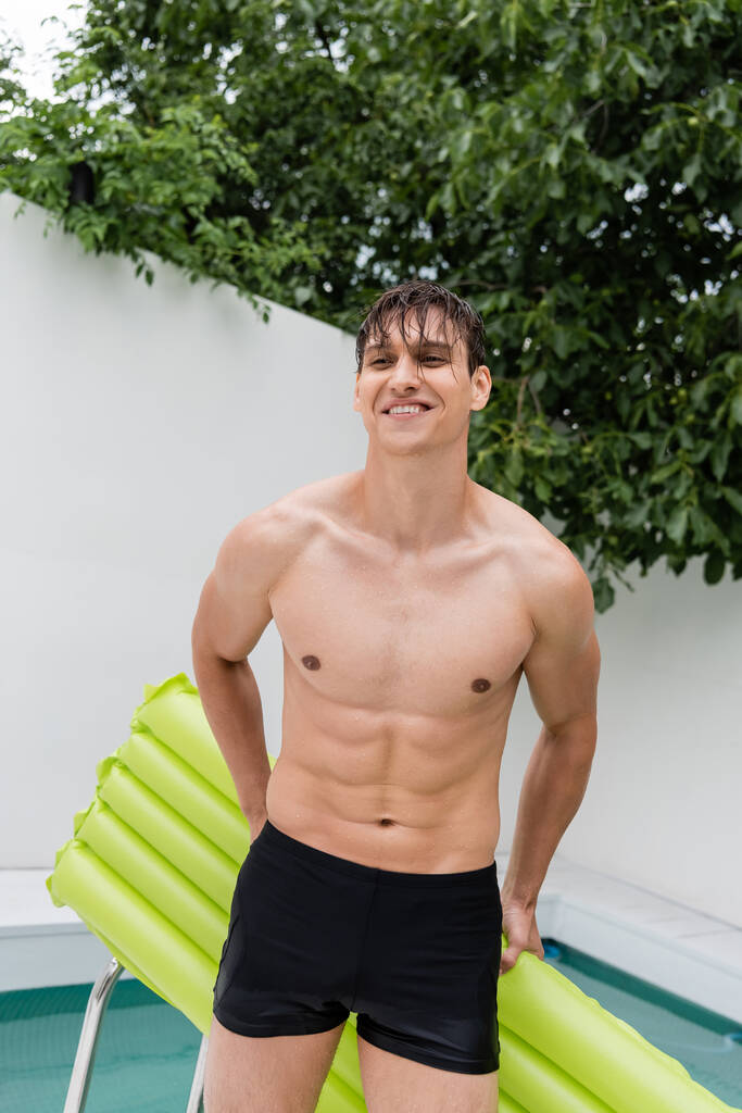 cheerful man in swimming trunks standing with swimming mattress outdoors - Photo, Image