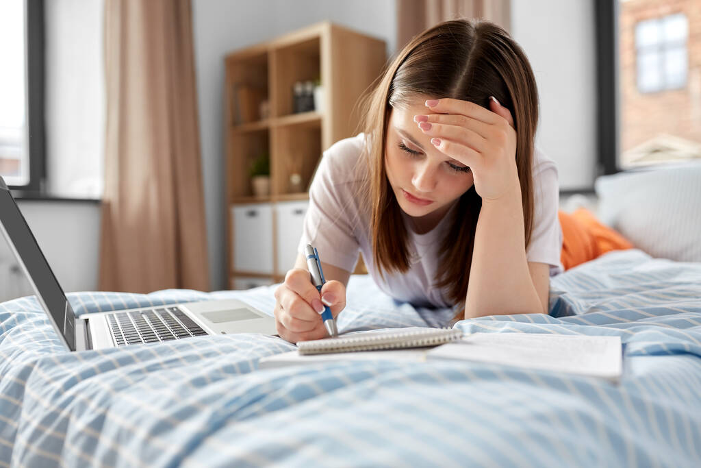 Schule, Bildung und Stresskonzept - müdes Teenager-Studentenmädchen mit Laptop und Notizbuch zu Hause im Bett - Foto, Bild