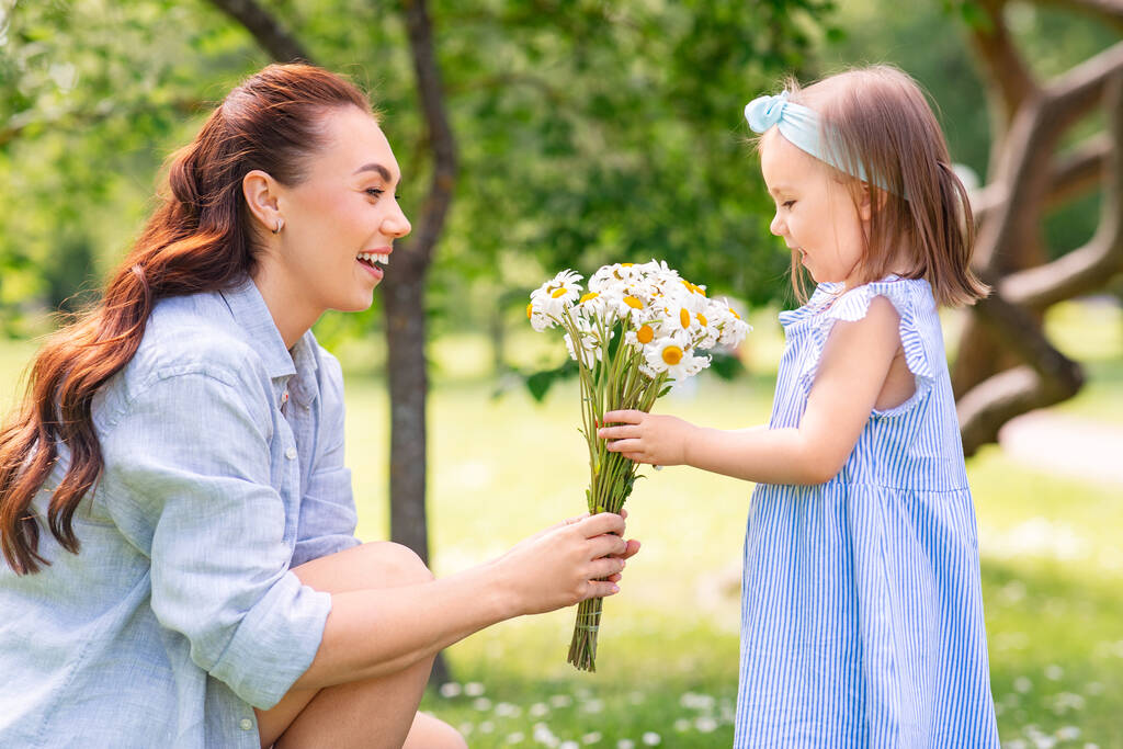 family, motherhood and people concept - happy mother with little daughter with chamomile flowers at summer park or garden - 写真・画像