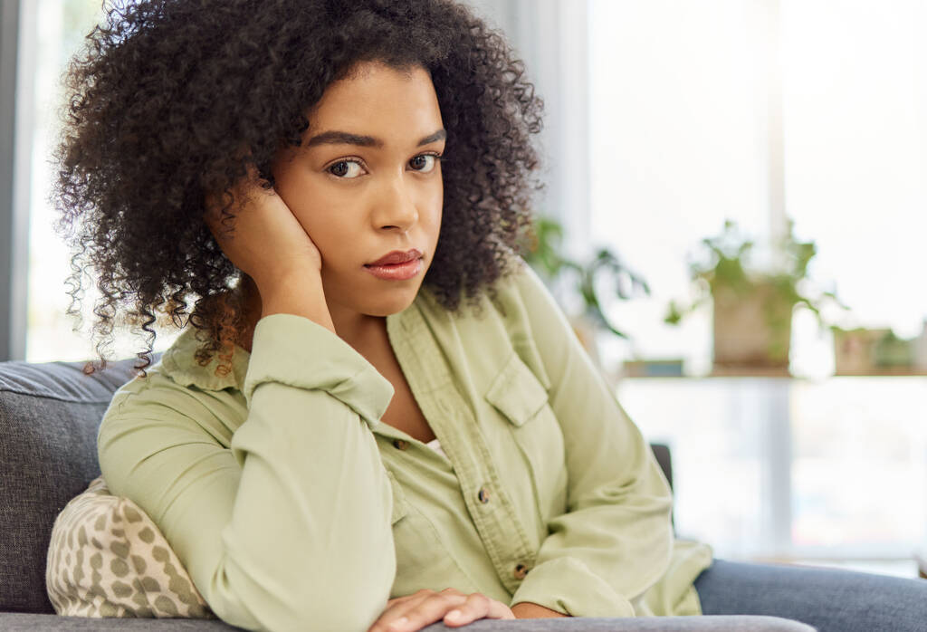 Young mixed race woman sitting on the couch alone at home. One unhappy hispanic female looking bored sitting at home. Woman with a curly afro sulking in the lounge at home. - Photo, image