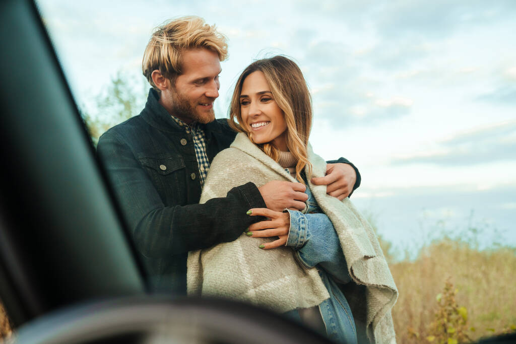 White mid couple smiling and hugging while standing by car during trip - Foto, Imagem