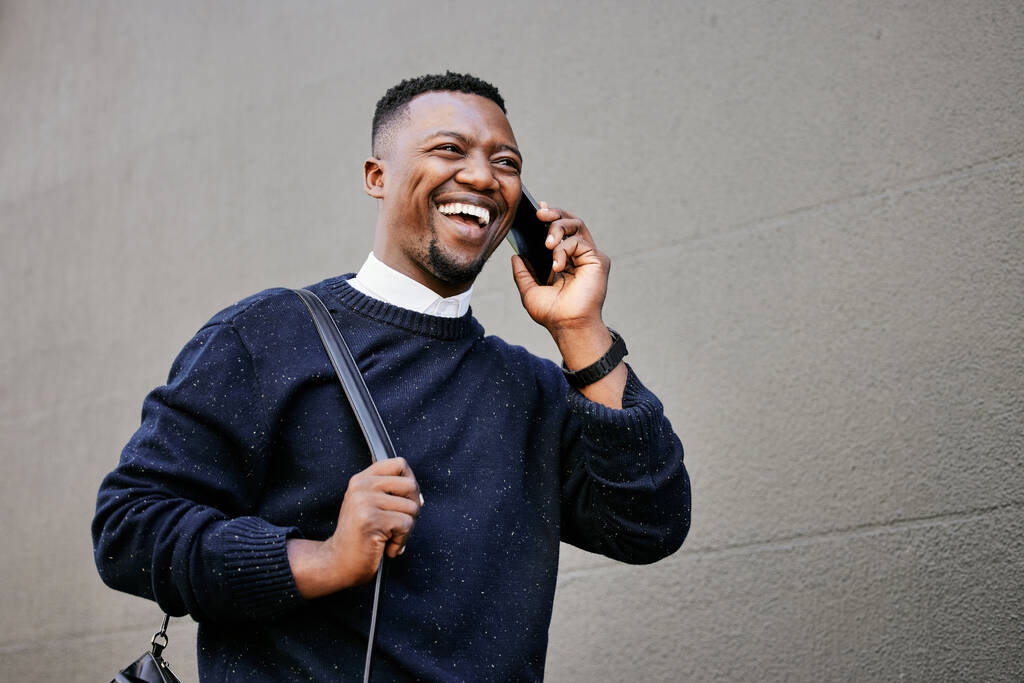 Африканский американец разговаривает по телефону со своим мобильным устройством возле здания в течение дня, улыбаясь Молодой черный мужчина разговаривает по телефону во время поездки на работу. - Фото, изображение