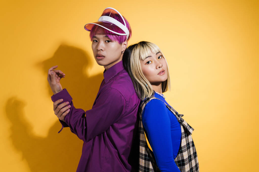 Азиатская пара с разноцветными волосами, позирующие спина к спине изолированы над желтой стеной - Фото, изображение