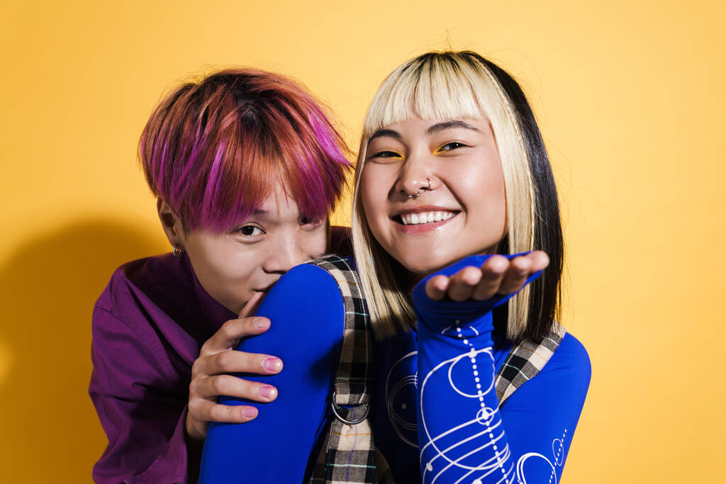 Азиатская пара с разноцветными волосами, улыбающаяся, держа пространство, изолированное над желтой стеной - Фото, изображение