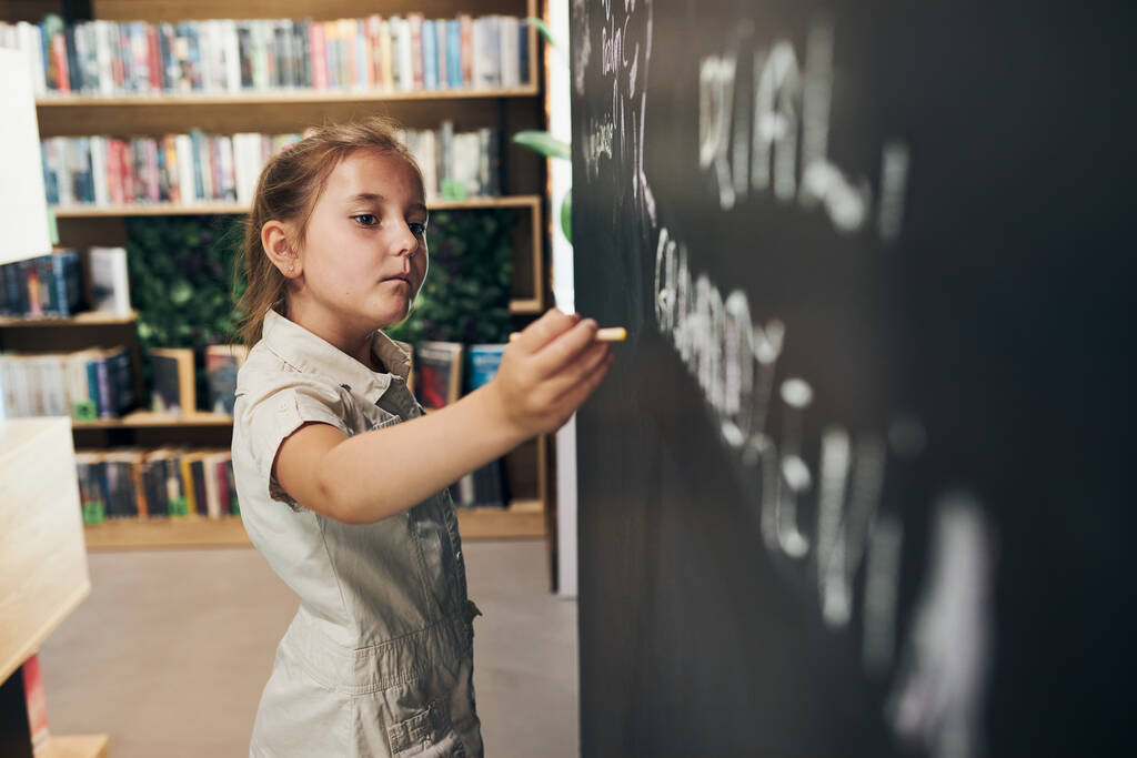 Little girl writing on blackboard. Smart student put solve on chalkboard. Back to school. Child having class. Schoolgirl learning at primary school. Elementary education - Photo, Image