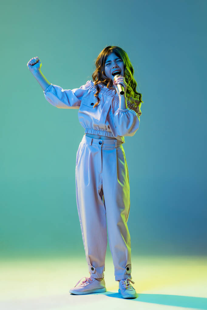 Музыкант, певец. Модная маленькая девочка, малыш позирует на голубом фоне в белом неоновом свете. Детские эмоции, мода, красота, возвращение в школу и реклама - Фото, изображение