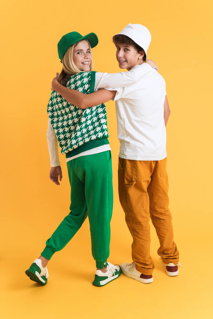White girl and boy laughing while hugging together isolated over yellow background - Φωτογραφία, εικόνα
