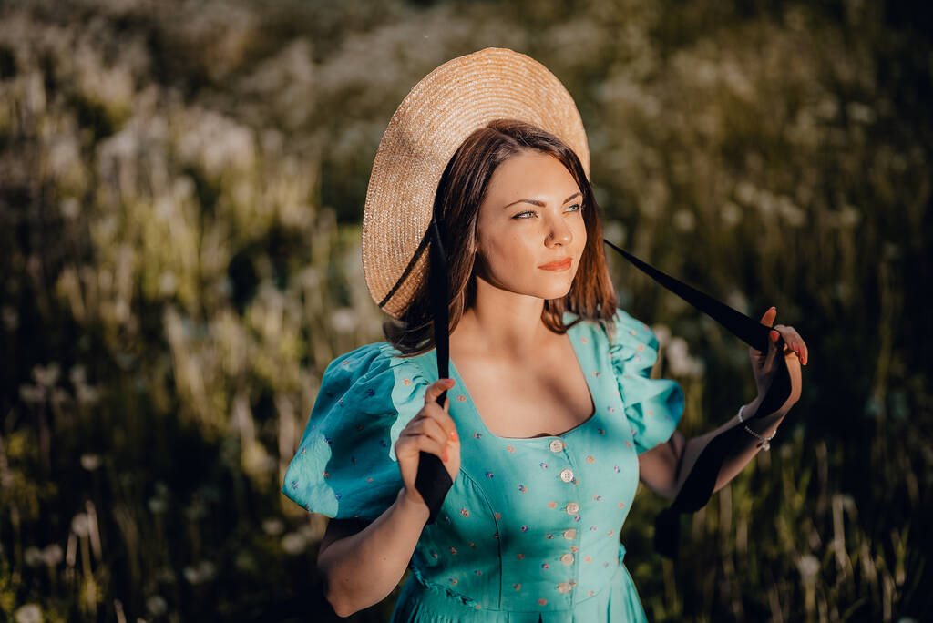 Young stylish woman in vintage dress and straw hat alone on nature in countryside. Carefree lifestyle, romantic girl. Retro fashionista like from novel. High quality photo - Photo, Image