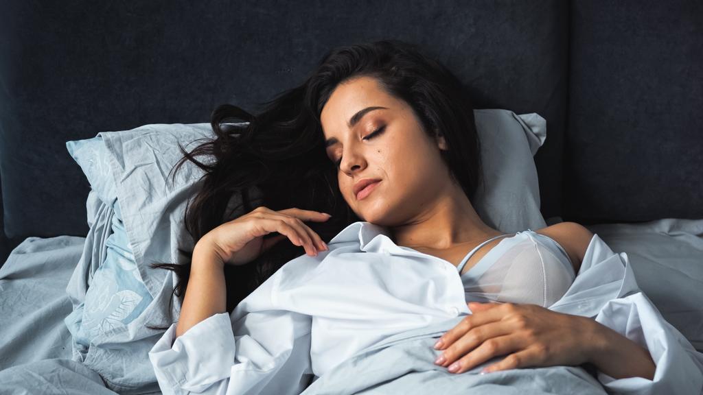 młoda kobieta z zamkniętymi oczami śpiąca w biustonoszu i koszuli  - Zdjęcie, obraz