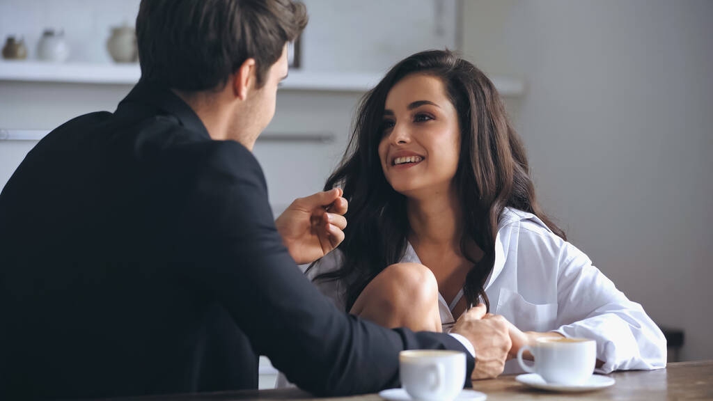 businessman talking with happy girlfriend in white shirt and holding hands near cups of coffee - Photo, Image
