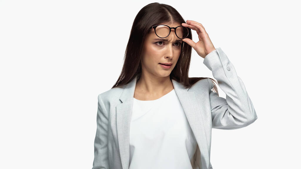 confused businesswoman in grey blazer adjusting eyeglasses isolated on white - Fotoğraf, Görsel