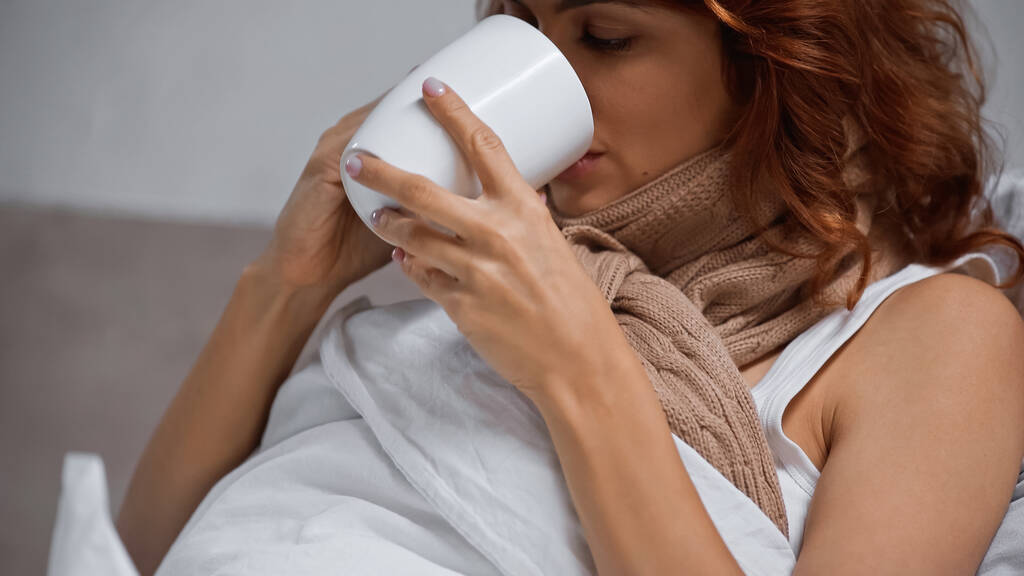 sick woman in scarf holding cup and drinking beverage at home - Φωτογραφία, εικόνα