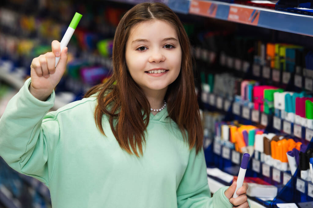 cheerful girl looking at camera while holding felt pens in stationery shop - 写真・画像