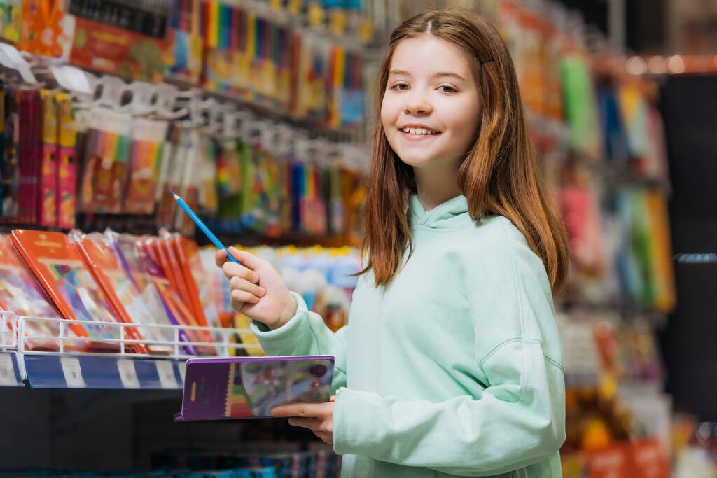 joyful girl with pencil set smiling at camera in stationery shop - Photo, image