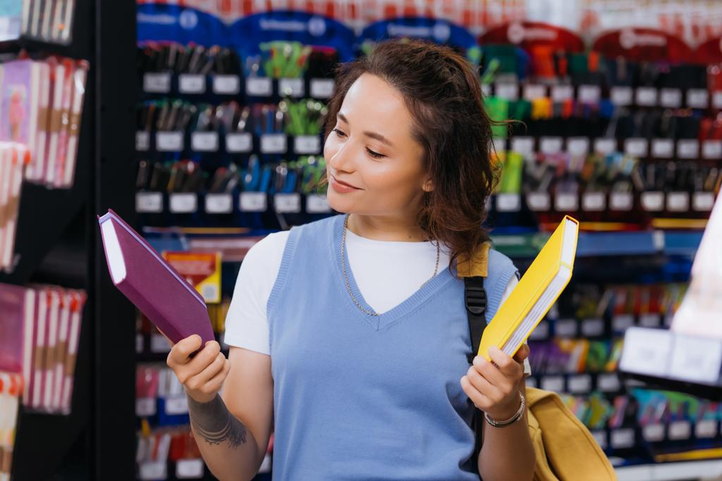 smiling tattooed student choosing copybooks in blurred stationery store - Foto, imagen