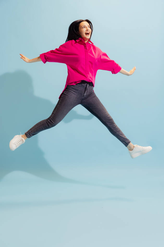 Happiness. Young beautiful excited woman in casual style outfit jumping isolated on blue background. Concept of beauty, art, fashion, youth, healthy lifestyle. Copyspace for ads, text, sales offer. - Foto, Bild