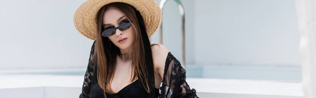 Fashionable woman in swimsuit and straw hat looking at camera at resort, banner  - Foto, immagini