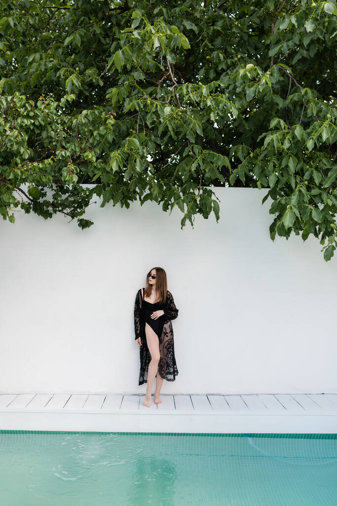 Stylische Frau im Badeanzug steht in der Nähe von Wand und Schwimmbad  - Foto, Bild