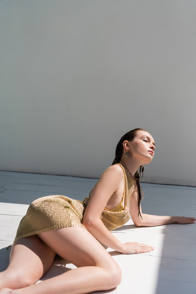 junge Frau in stylischem Sommerkleid liegt mit geschlossenen Augen auf weißer Oberfläche  - Foto, Bild