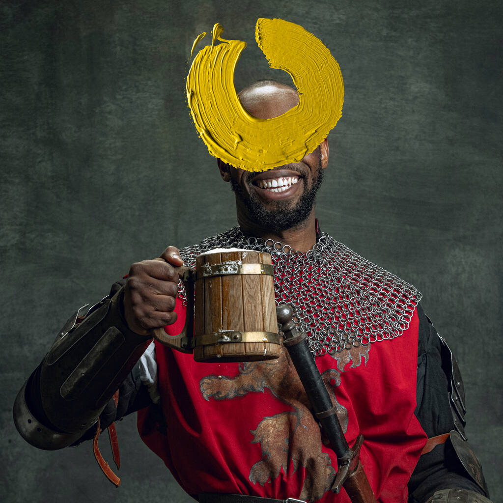 Modern art design. Young man as medieval warrior, knight isolated on dark vintage background. Random stroke of yellow paint on his face. Human emotions, comparison of eras, art, new vision concept. - Foto, imagen