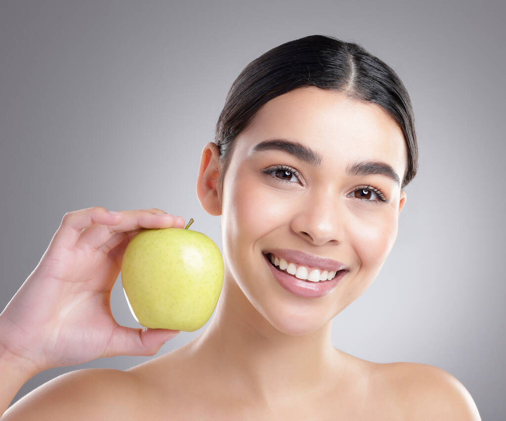 Add an apple to your everyday diet. Studio portrait of an attractive young woman posing with an apple against a grey background - Foto, Imagen