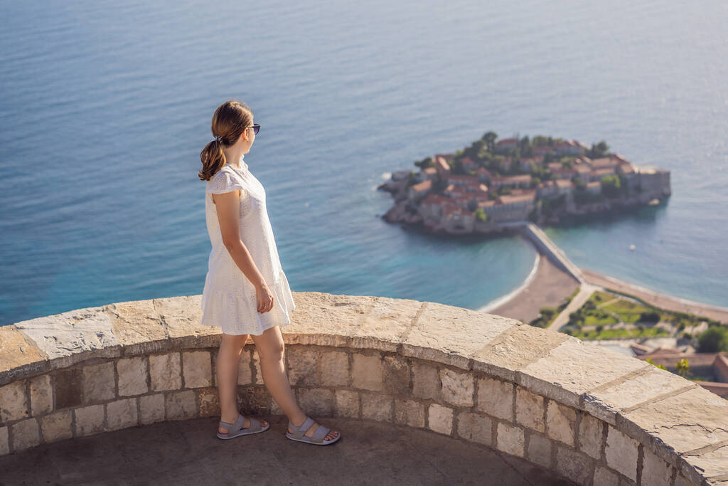 Vrouw toerist op de achtergrond van een prachtig uitzicht op het eiland St. Stephen, Sveti Stefan aan de Budva Riviera, Budva, Montenegro. Reizen naar Montenegro. - Foto, afbeelding