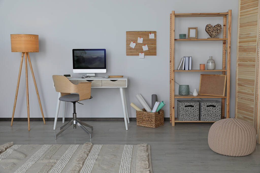 Stylish room interior with comfortable workplace and shelving unit near white wall - Фото, изображение