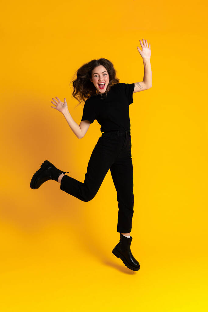 Valkoinen innoissaan nainen musta t-paita tekee hauskaa ja hyppää eristetty yli keltainen tausta - Valokuva, kuva