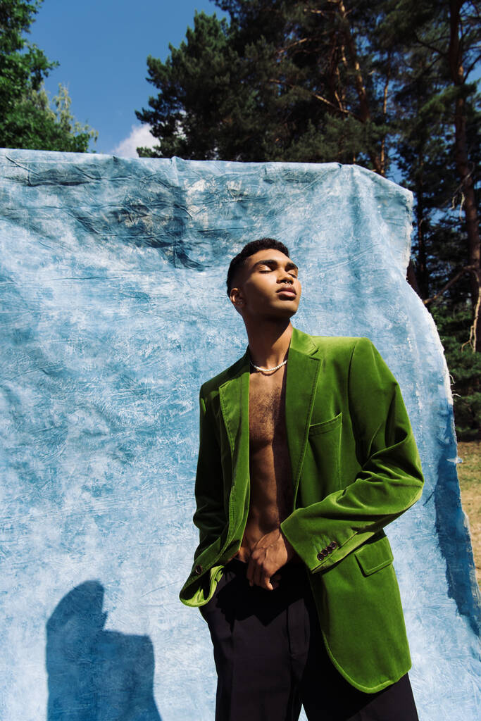 african american man in green velvet blazer posing with closed eyes near blue cloth - Zdjęcie, obraz