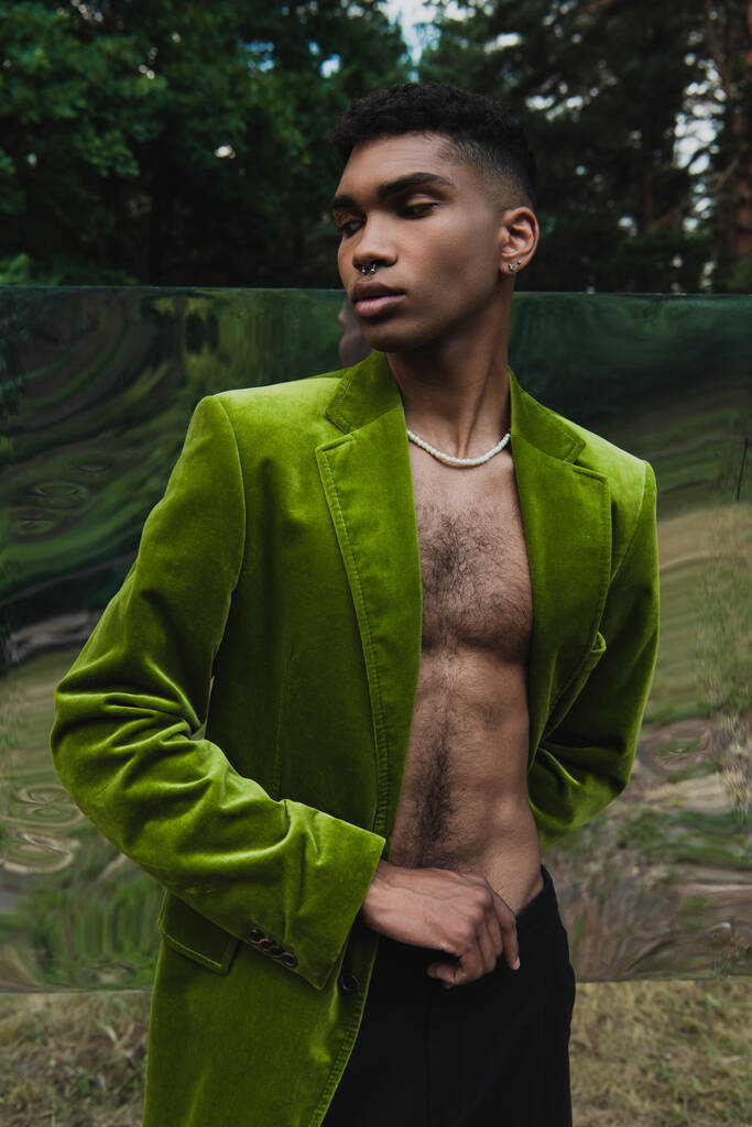 divatos afro-amerikai férfi gyöngyök és bársony blézer pózol erdő közelében rugalmas tükör - Fotó, kép