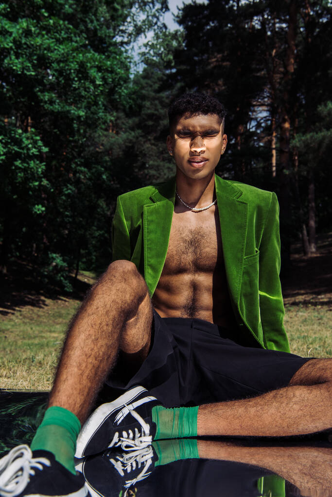 african american man in green blazer and black shorts sitting with closed eyes in park on reflective surface - Φωτογραφία, εικόνα