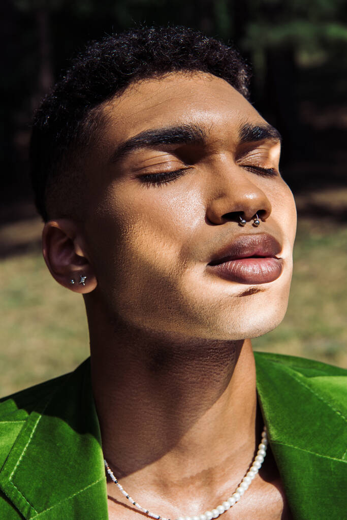 portrait of african american man with closed eyes and piercing in sunshine outdoors - Fotó, kép