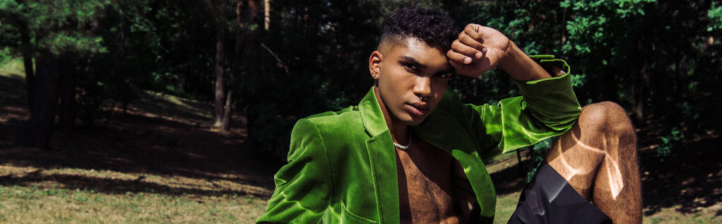 Yeşil kadife ceketli modaya uygun Afro-Amerikan adam parkta otururken kameraya bakıyor. - Fotoğraf, Görsel